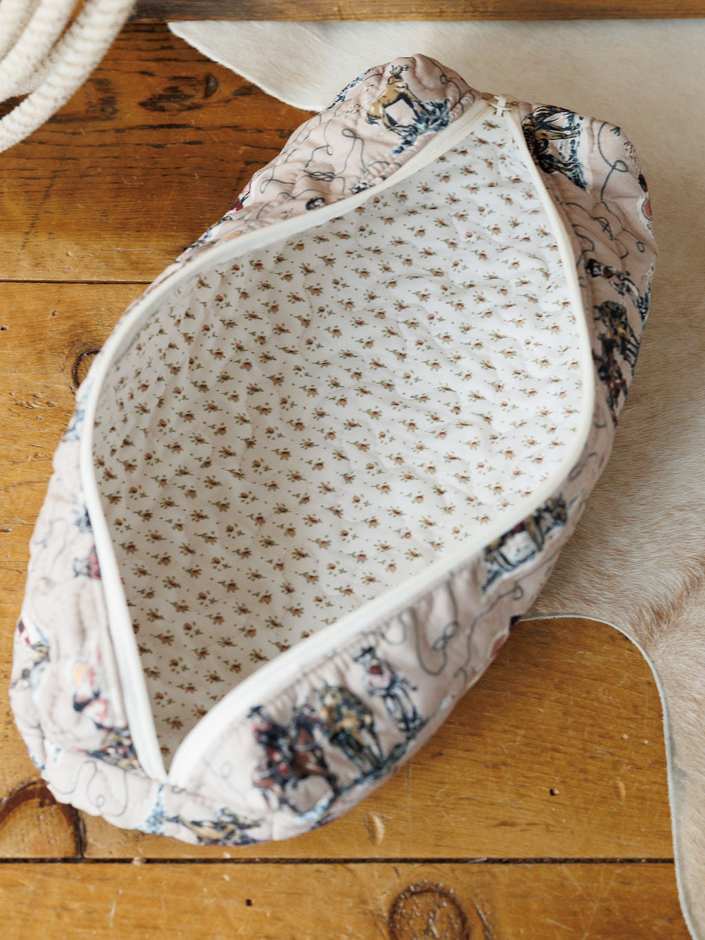 The Montana Summer Collection zippered pouch by Savannah Sevens western life&style features a light floral print interior, shown open on wood with a hint of cowhide rug beneath.