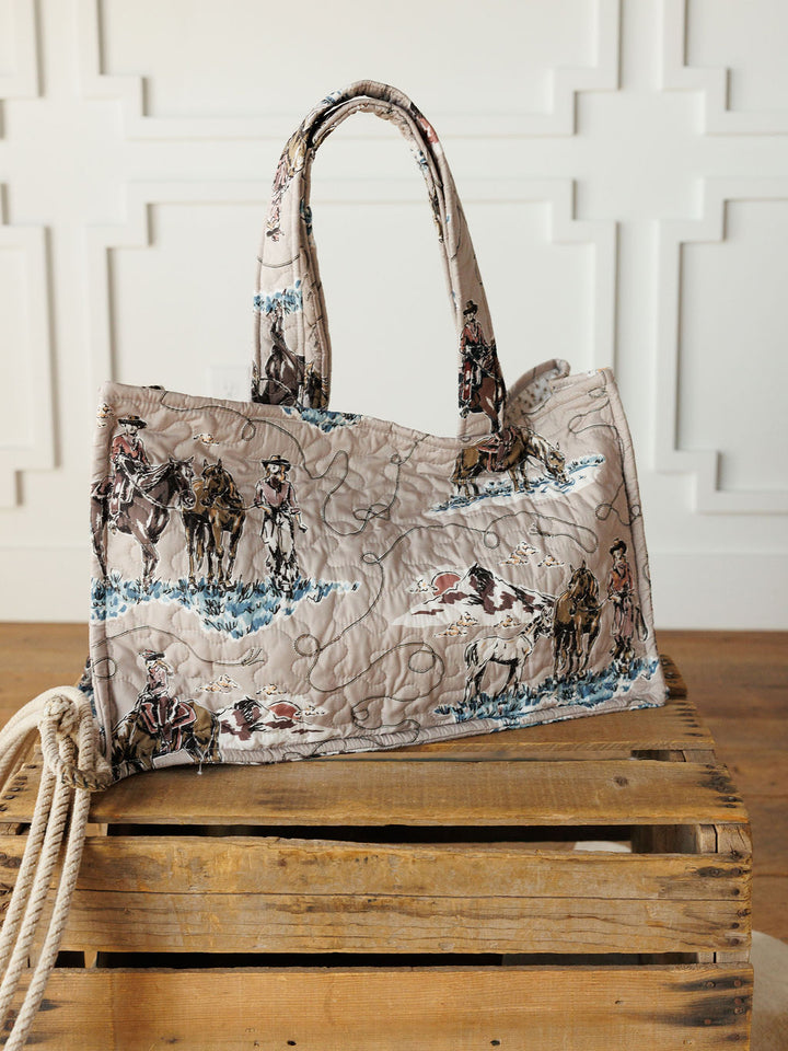 The Montana Summer Collection by Savannah Sevens western life&style features a handmade quilted bag set with cowboy and horse prints, shown on a crate with rope against a white paneled wall, highlighting its unique western style.