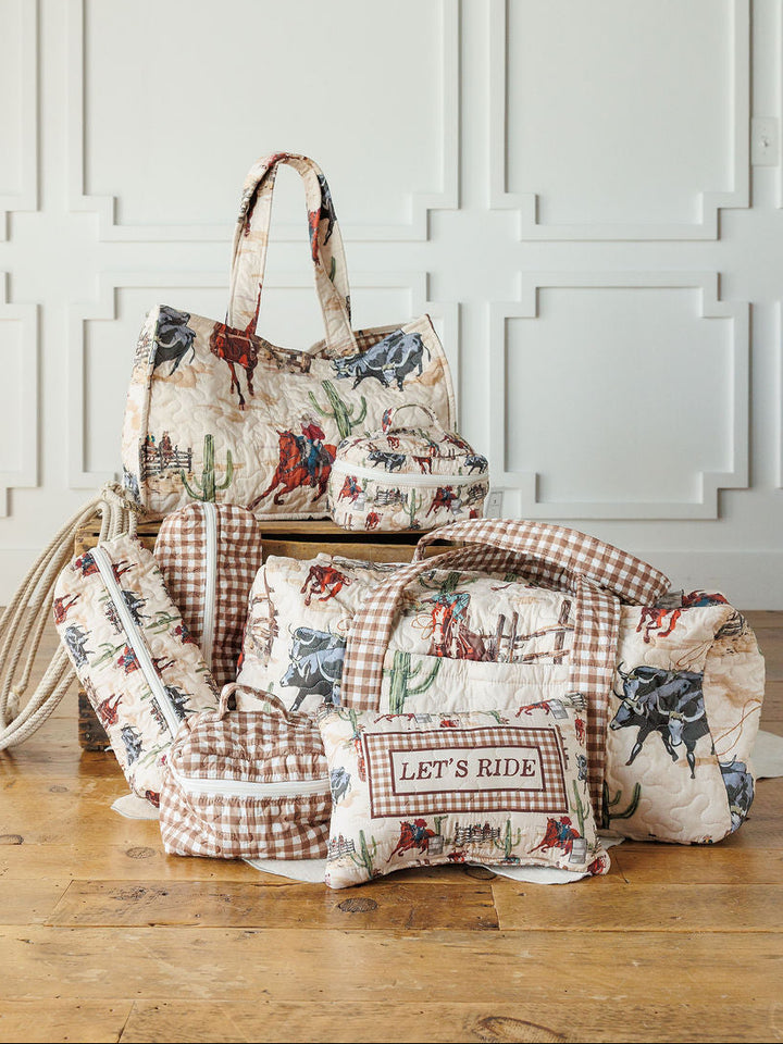 The Cowgirl Gingham Collection by Savannah Sevens western life{&}style features quilted travel bags and a “LET’S RIDE” pillow with cowboy, horse, cactus, and vintage gingham prints, arranged on a wooden floor against a white paneled wall.