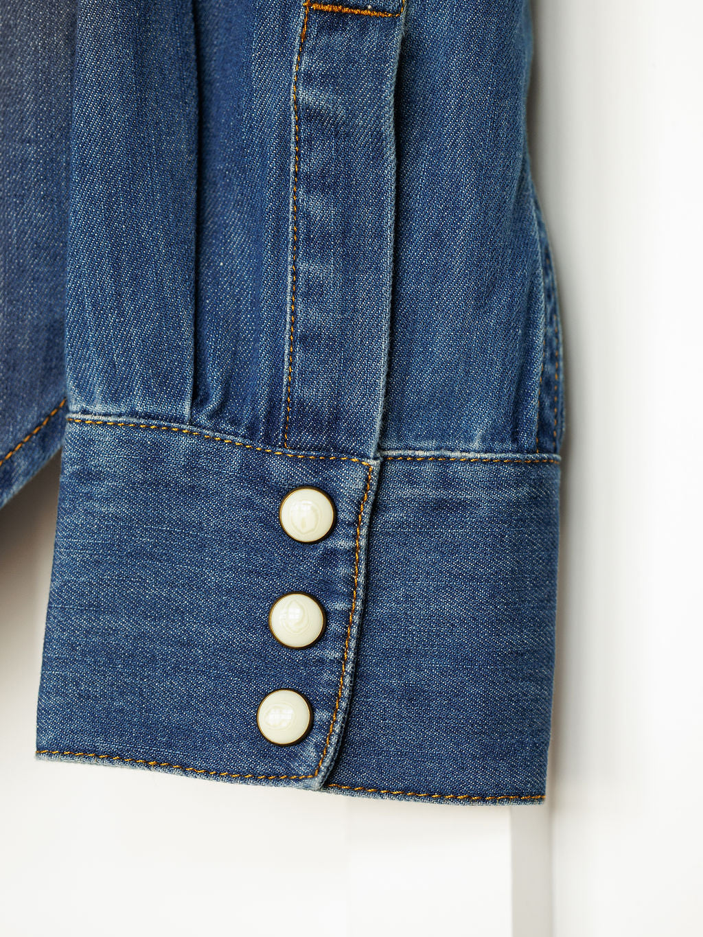 Close-up of The Tekamah by Savannah Sevens western life{&}style, featuring a long sleeve cuff in blue textured denim with orange stitching and three white buttons. Classic denim details highlight its timeless western style.