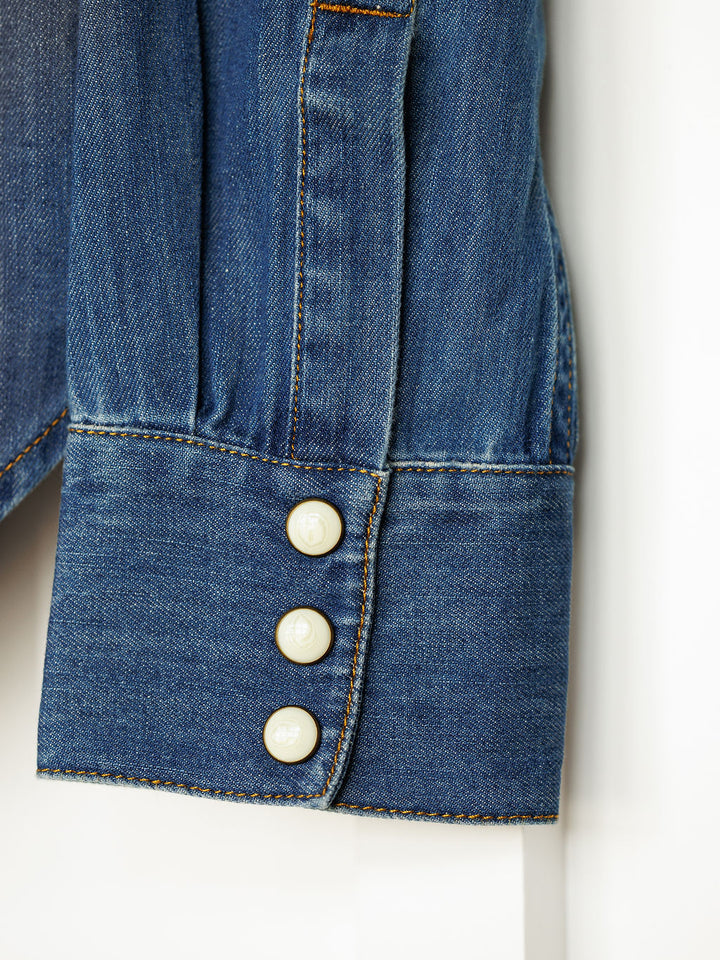 Close-up of The Tekamah by Savannah Sevens western life{&}style, featuring a long sleeve cuff in blue textured denim with orange stitching and three white buttons. Classic denim details highlight its timeless western style.