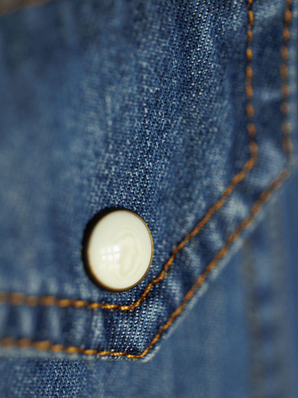 Close-up of The Tekamah by Savannah Sevens western life{&}style, featuring blue denim, bronze stitching, and a white pearl snap button on this classic western long sleeve shirt.
