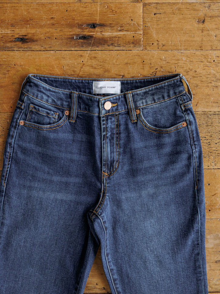 A pair of Savannah Sevens western life{&}style The Camryn Premier Rise Slim Straight Leg Jeans with dark wash, bronze stitching, and a white waistband label displayed flat on a wooden floor.