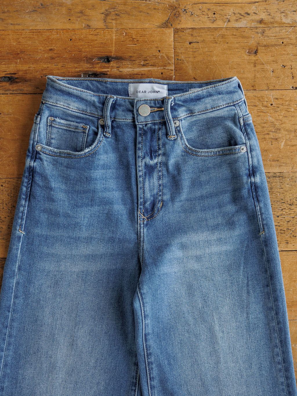 A pair of The Slayden High Rise Wide Leg Jeans by Savannah Sevens western life{&}style, featuring front pockets and a button closure, laid flat on a wooden floor.