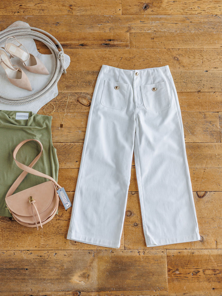 The Owasso by Savannah Sevens western life{&}style: white denim wide leg crop pants with gold buttons, shown laid flat with beige heels, a round beige purse, green sleeveless top with tag, necklace, and a light woven bag.