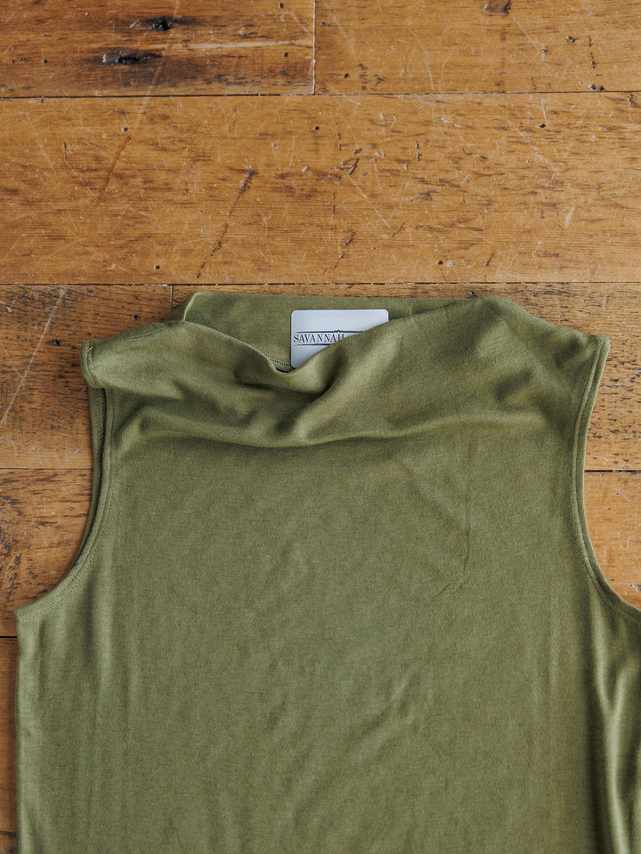 The Mandan by Savannah Sevens western life{&}style, a sleeveless olive cowl neck tri-blend top, is laid flat on a wooden surface with its inner label partially visible.