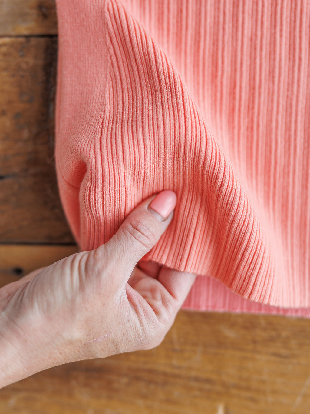 A hand  lifts the ribbed fabric of The Lasara v-neck sleeveless top by Savannah Sevens western life{&}style on a wooden surface.