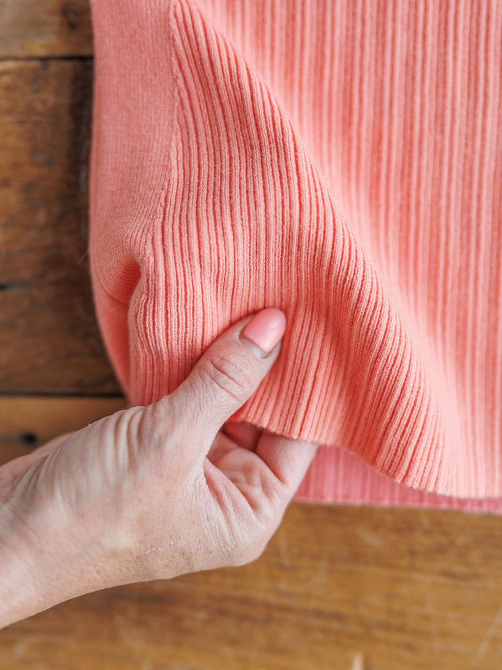 A hand  lifts the ribbed fabric of The Lasara v-neck sleeveless top by Savannah Sevens western life{&}style on a wooden surface.