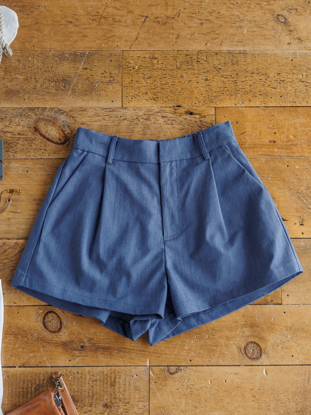 The Lenox high-waisted denim blue shorts by Savannah Sevens western life{&}style, made from a cotton blend with belt loops, are shown laid flat on a wooden surface.
