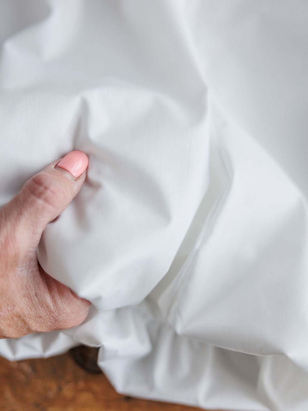 A hand gently grasps The Panora sleeveless white top by Savannah Sevens western life{&}style, creating soft folds and wrinkles in the cotton blend fabric.