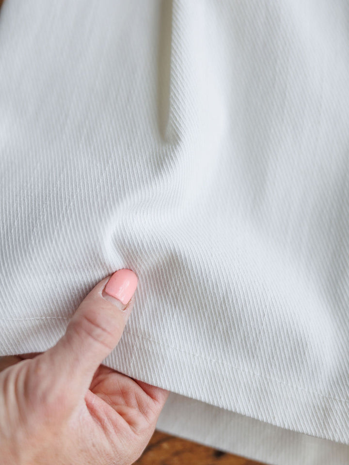 A hand pinches the textured, off-white fabric of The Morley high waisted cotton blend shorts by Savannah Sevens western life{&}style, highlighting its fine diagonal ribbing.