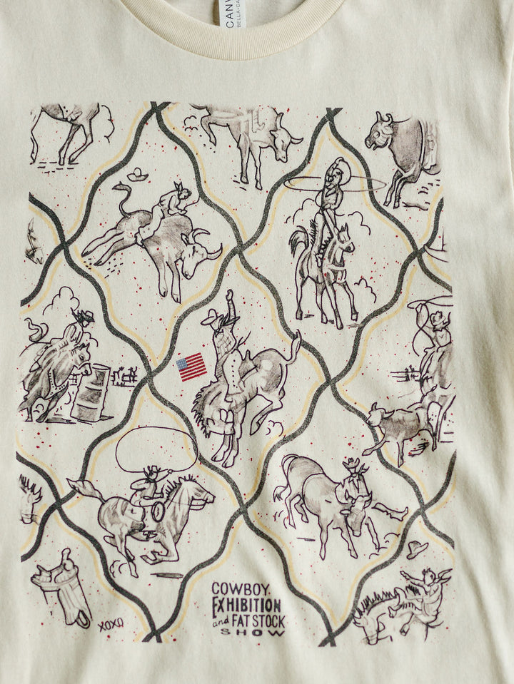 The Cowboy Exhibition tee by Savannah Sevens western life{&}style is cream-colored and features line-drawn cowboys riding bulls, roping cattle, rodeo tricks, an American flag, and the text COWBOY EXHIBITION and FAT STOCK SHOW.