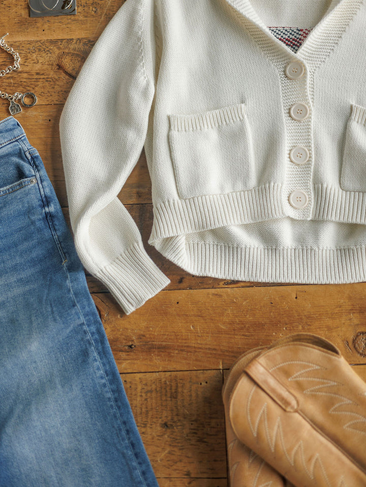 The American Classic {Exclusive} by Savannah Sevens western life{&}style features a cream 100% cotton cardigan with pockets, blue denim jeans, and tan cowboy boots displayed on a wooden floor.