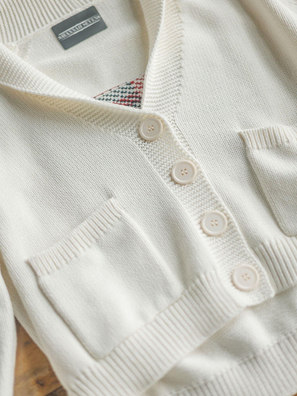 A close-up of The American Classic {Exclusive} cardigan by Savannah Sevens western life{&}style: cream-colored, 100% cotton, four beige buttons, two front pockets, textured collar, and a peek of colorful patterned fabric at the neckline.