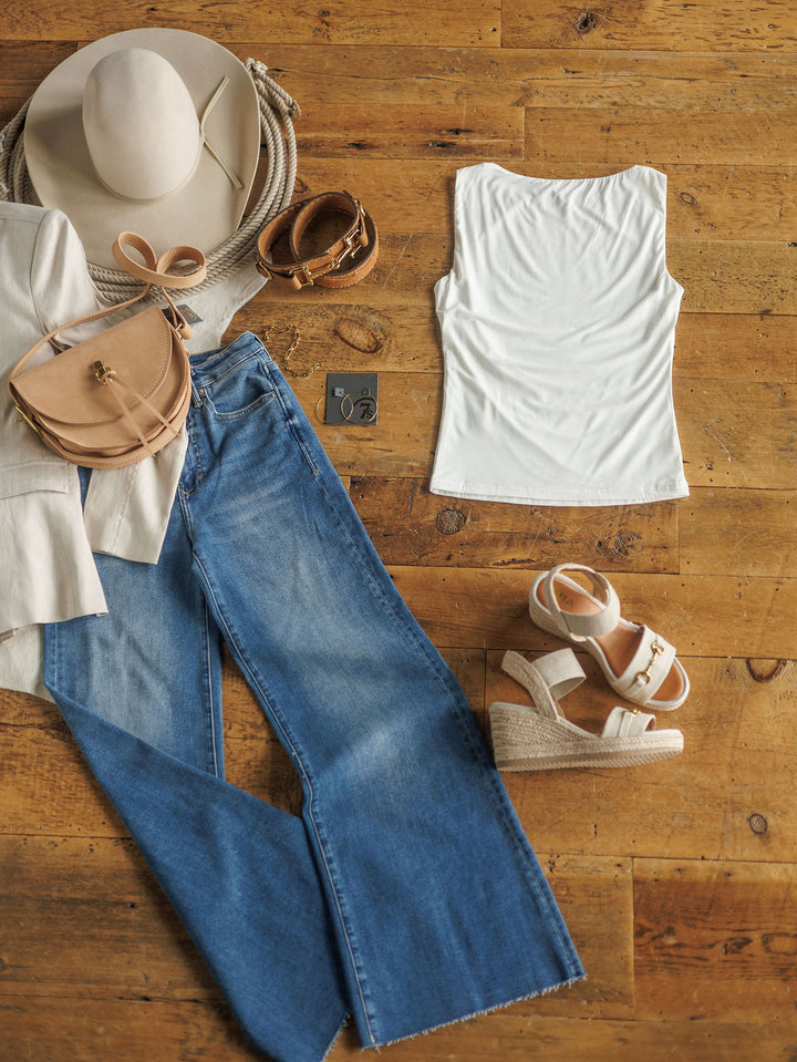 Flat lay of The Renton tank by Savannah Sevens western life{&}style, styled with blue jeans, a white blazer, beige hat, tan crossbody bag, wedge sandals, belt, sunglasses, and jewelry on a wooden floor.