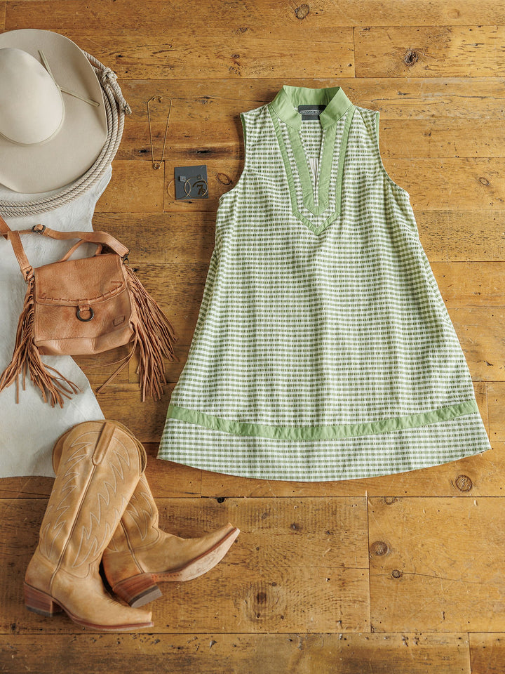 The Halstad by Savannah Sevens western life{&}style is a sleeveless green and white gingham dress, styled with tan cowboy boots, a fringed suede bag, a white wide-brimmed hat, and a turquoise belt buckle for a young contemporary vibe.