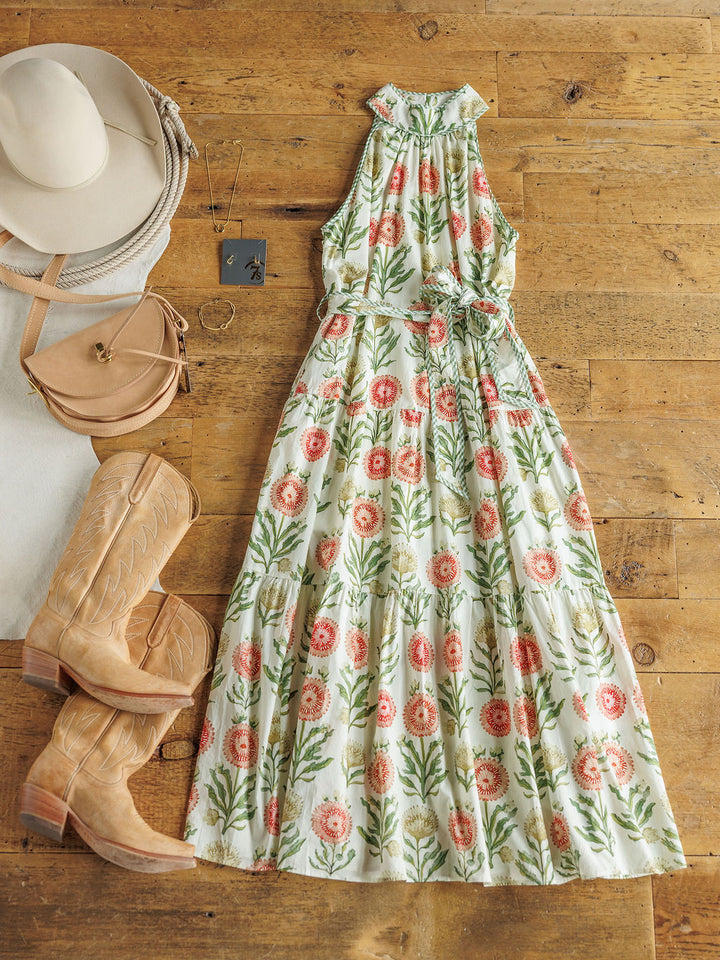 The Marianna by Savannah Sevens western life{&}style, a cotton floral full-length maxi dress with a tie waist, is styled with tan cowboy boots, a beige crossbody bag, wide-brimmed hat, white scarf, and square pendant necklace.