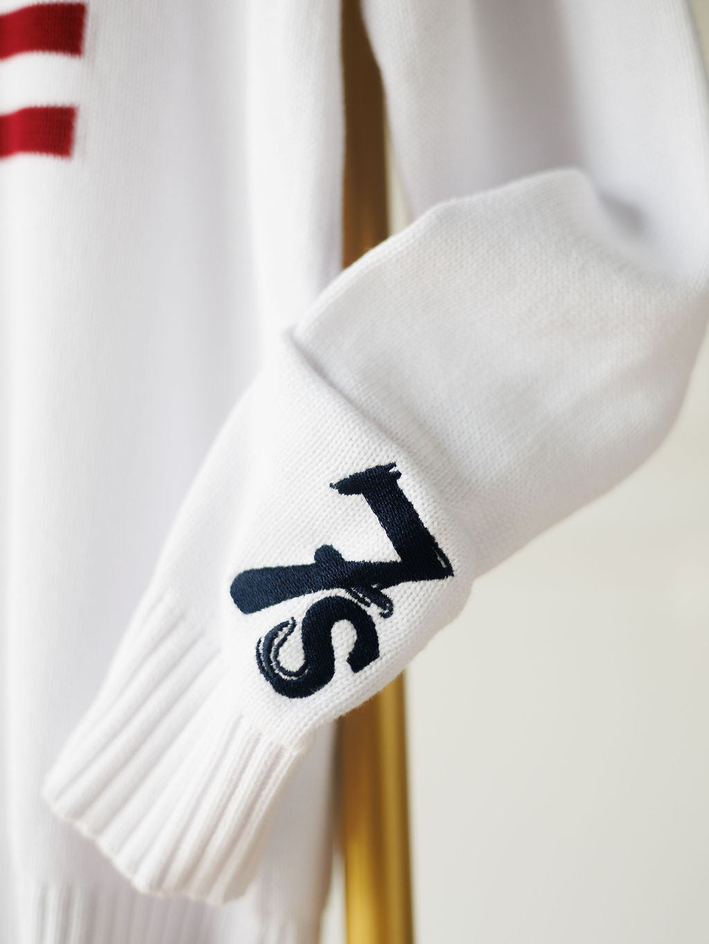 A close-up of The American West {Exclusive} white knit sleeve by Savannah Sevens western life{&}style, featuring a navy 7s logo near the cuff —a signature touch of the brand.