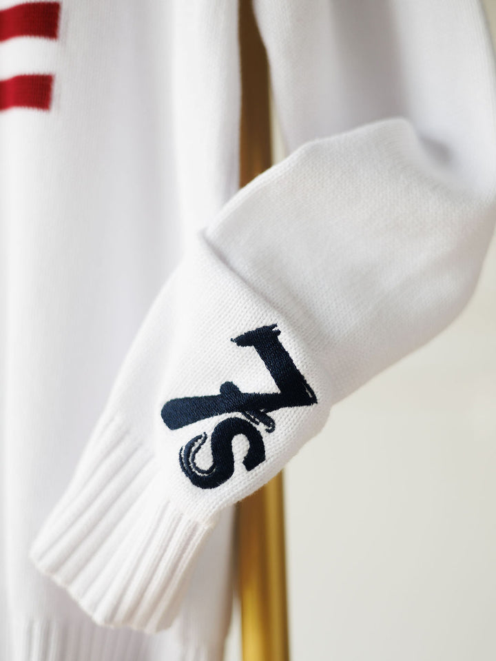 A close-up of The American West {Exclusive} white knit sleeve by Savannah Sevens western life{&}style, featuring a navy 7s logo near the cuff —a signature touch of the brand.