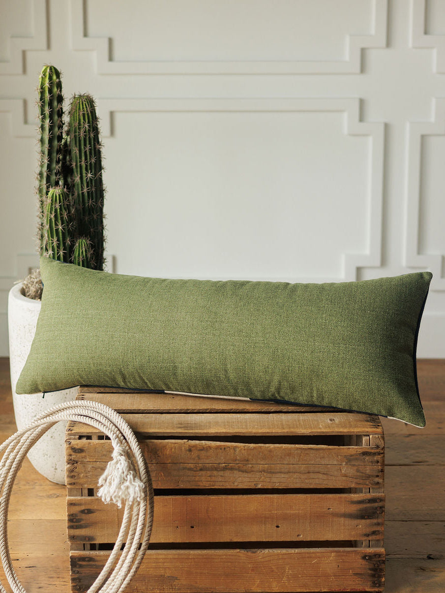 The Presidio Lumbar Pillow Cover in Midnight Navy by Savannah Sevens western life{&}style rests on a wooden crate next to a coiled rope and potted cactus, set against a white paneled wall.