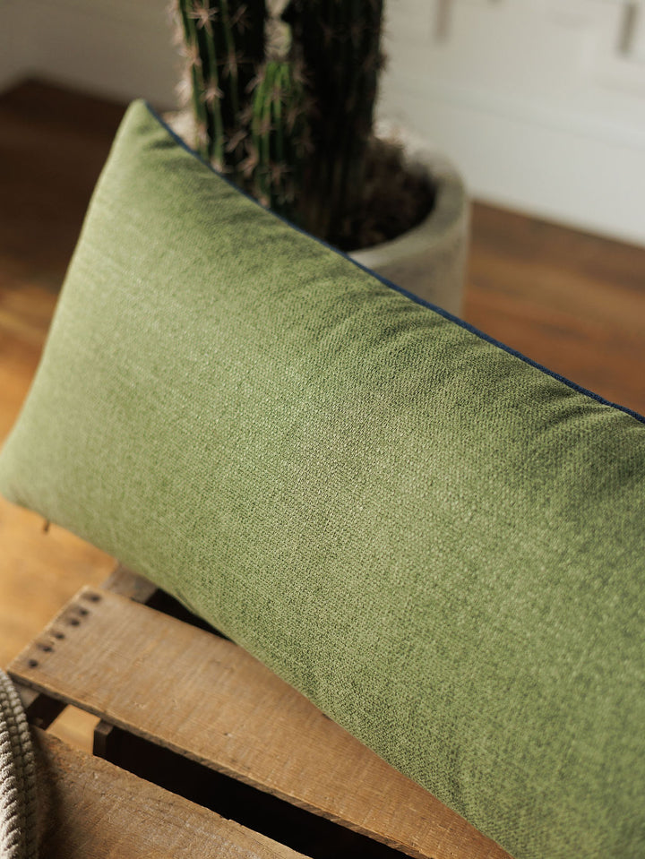 The Presidio Lumbar Pillow Cover in Midnight Navy from Savannah Sevens western life{&}style rests on a wooden surface, with a potted cactus in the background and sunlight illuminating the scene.