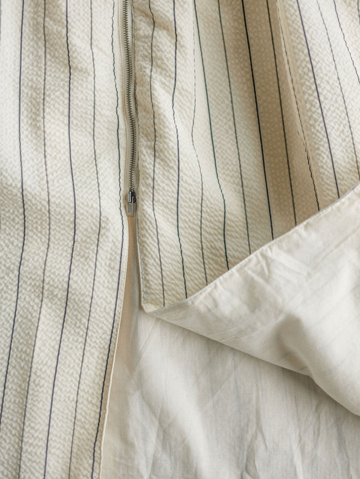 Close-up of The Palomar midi dress by Savannah Sevens western life{&}style, featuring white textured fabric with thin vertical blue stripes and a partial unzip revealing a smooth white lining.