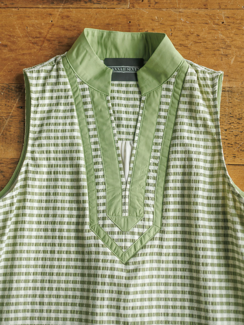 The Halstad by Savannah Sevens western life{&}style is a sleeveless green and white patterned blouse with a stand-up collar, V-neckline, and green trim, shown laid flat on a wooden surface.