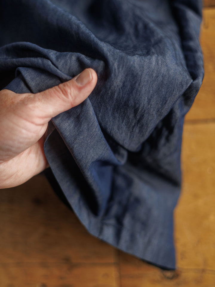 A hand holds The Meridan dark denim blue cotton blend fabric from Savannah Sevens western life{&}style, perfect for high waisted wide leg pants, over a wooden surface.