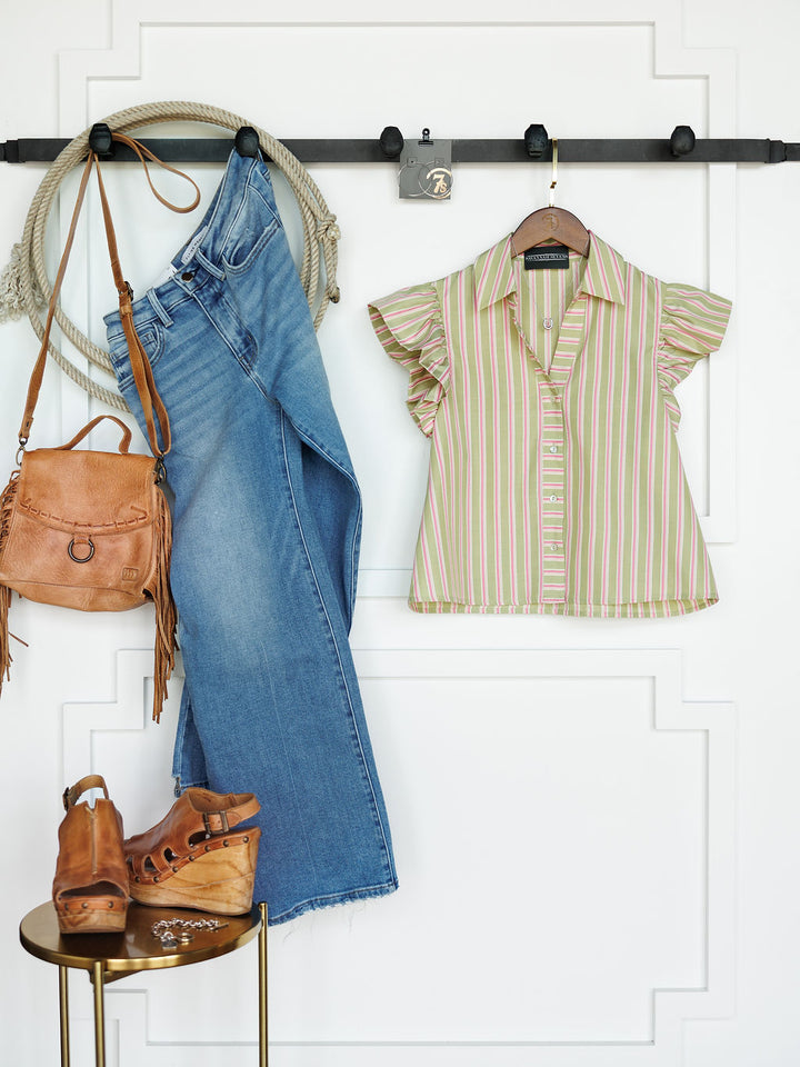 The Rayas by Savannah Sevens western life{&}style: blue jeans, striped button-up top, tan fringe handbag, and brown platform sandals displayed on a white wall with molding beside a small round gold table.