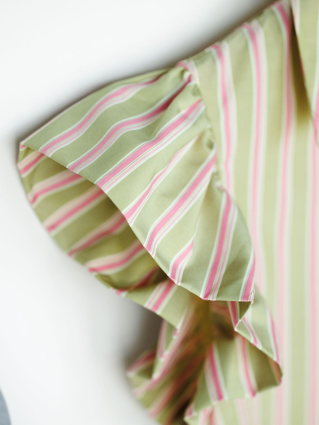 Close-up of the ruffled short sleeve on The Rayas sage pink blouse by Savannah Sevens western life{&}style, featuring white and pink vertical stripes. Soft fabric and flutter sleeve add a stylish, decorative touch.
