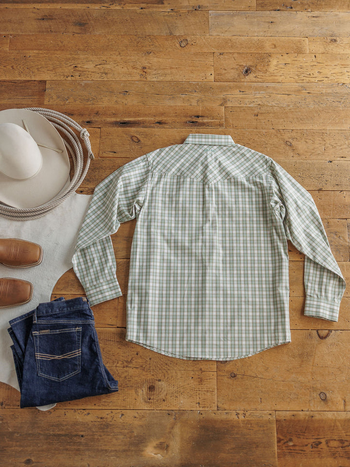 The Eastwood men's plaid snap shirt in green and white by Savannah Sevens western life&style is laid flat on a wooden floor beside blue jeans, brown shoes, a white cowboy hat, and a coiled rope.