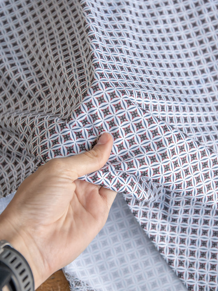 A hand holds up geometric diamond and star print fabric in white, light blue, black, and red. The person wears a black wristband and The Lyman {Men's} polo from Savannah Sevens western life{&}style.