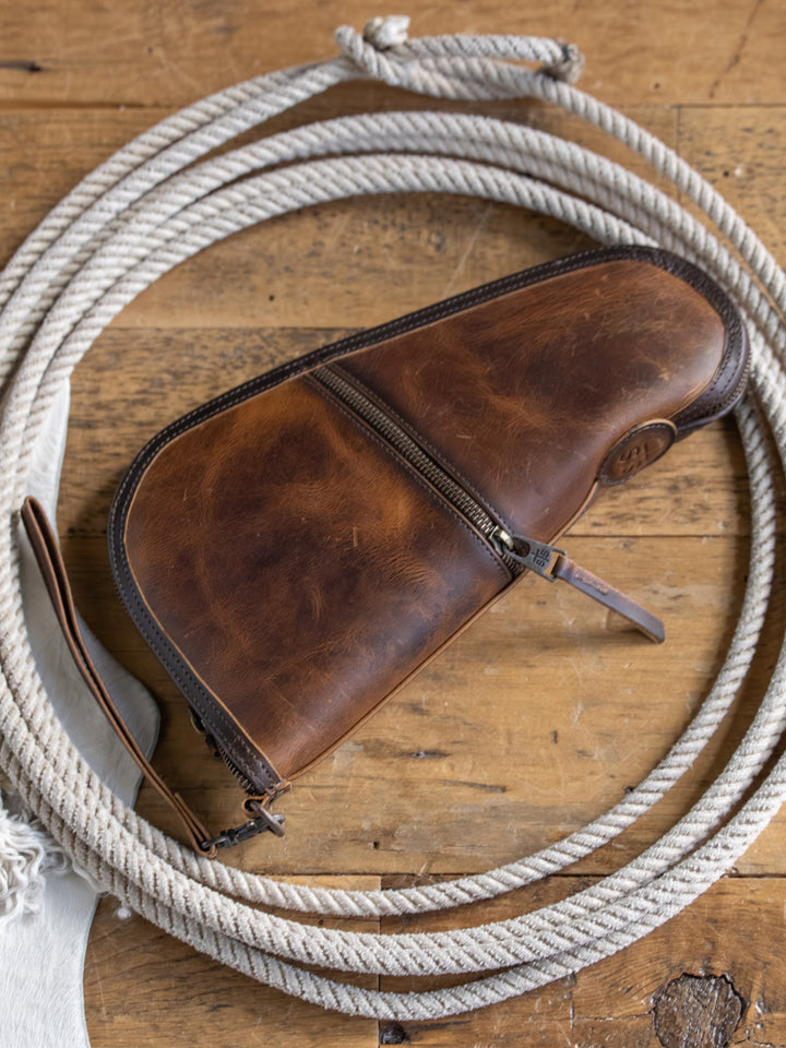 The Waynesboro Pistol Case from Savannah Sevens western life{&}style sits on a coiled rope atop wood, with a fringed white cloth partially visible nearby.