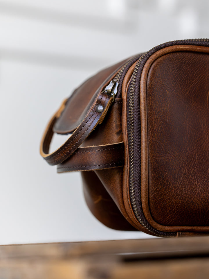 Close-up of the Wayneboro Shave Bag by Savannah Sevens western life{&}style, featuring detailed texture and stitching on full grain brown leather, zipper closure, and small handle. A light background highlights the bag’s craftsmanship.