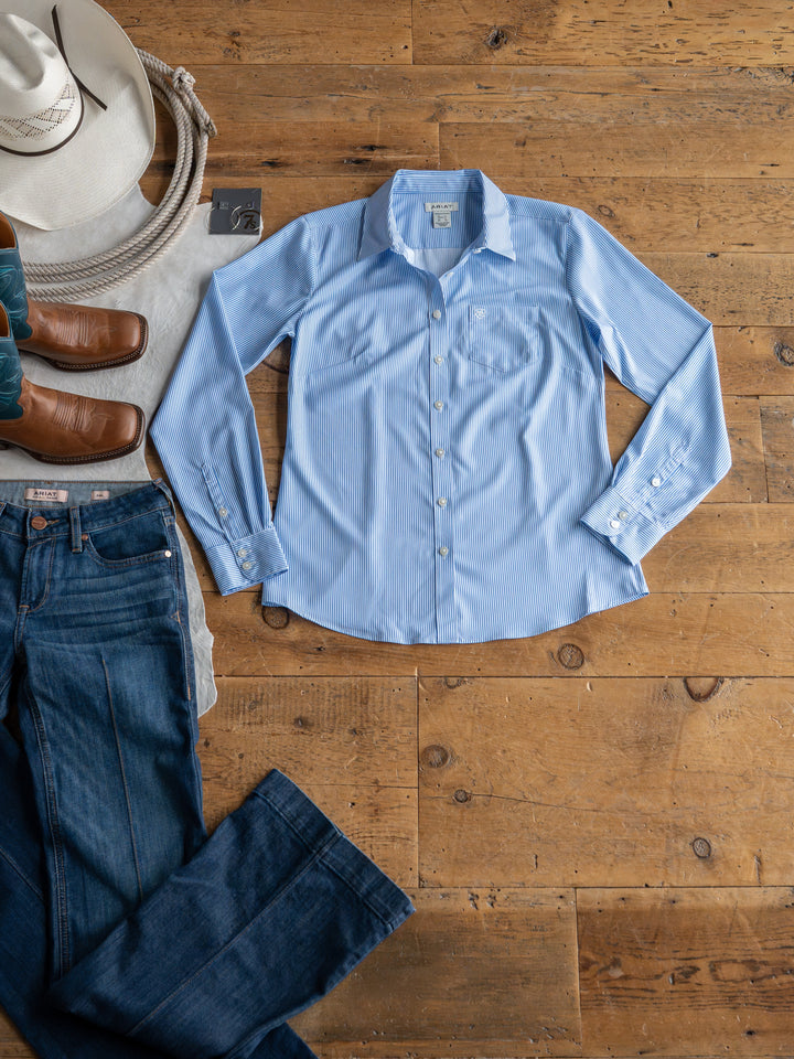 The Ellisville by Savannah Sevens western life{&}style, a light blue pinstripe button-up shirt, is laid flat on a wooden floor beside blue jeans, brown boots, a white hat, and a gray belt.