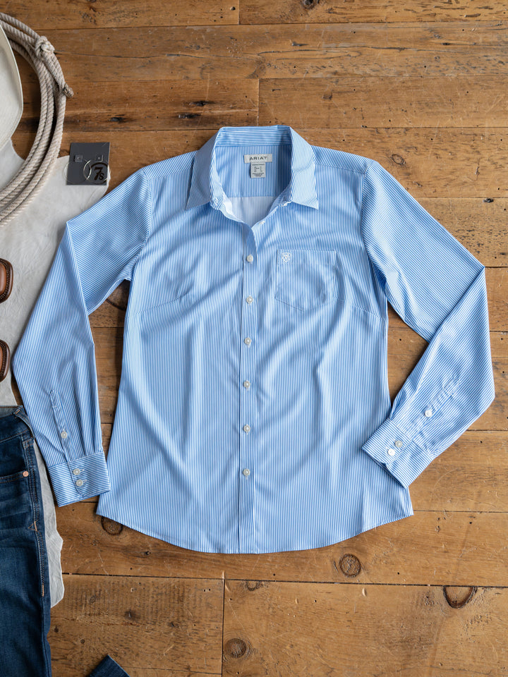 The Ellisville by Savannah Sevens western life{&}style: a light blue pinstripe, long-sleeve button-up shirt with subtle white stripes, displayed with jeans, sunglasses, and a white bag—stylish sun protection for any occasion.