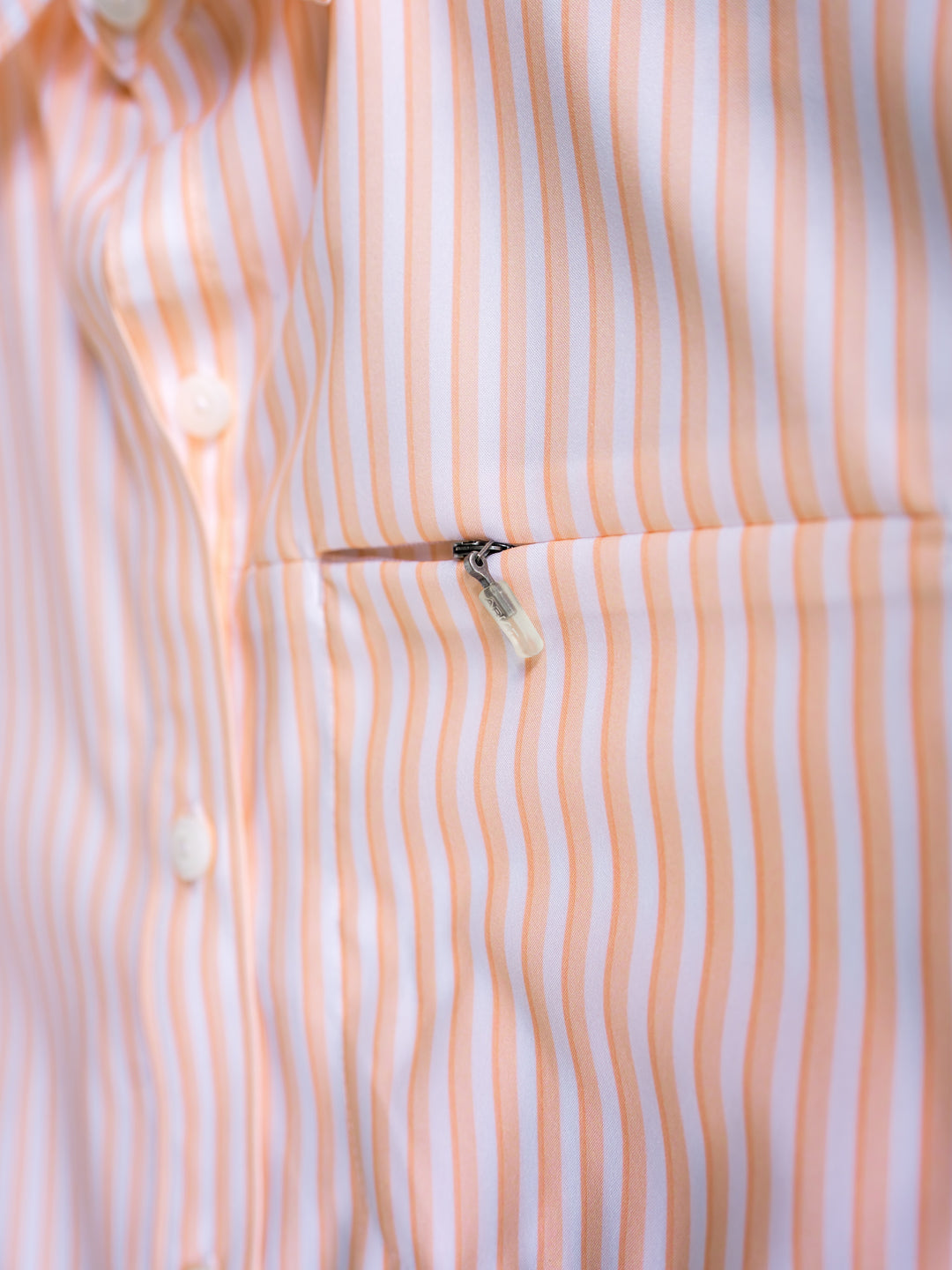 Close-up of The Lovilia shirt by Savannah Sevens western life{&}style with vertical peach and white stripes, white buttons, and a chest zippered pocket. This sun protection top offers moisture wicking comfort for all-day wear.