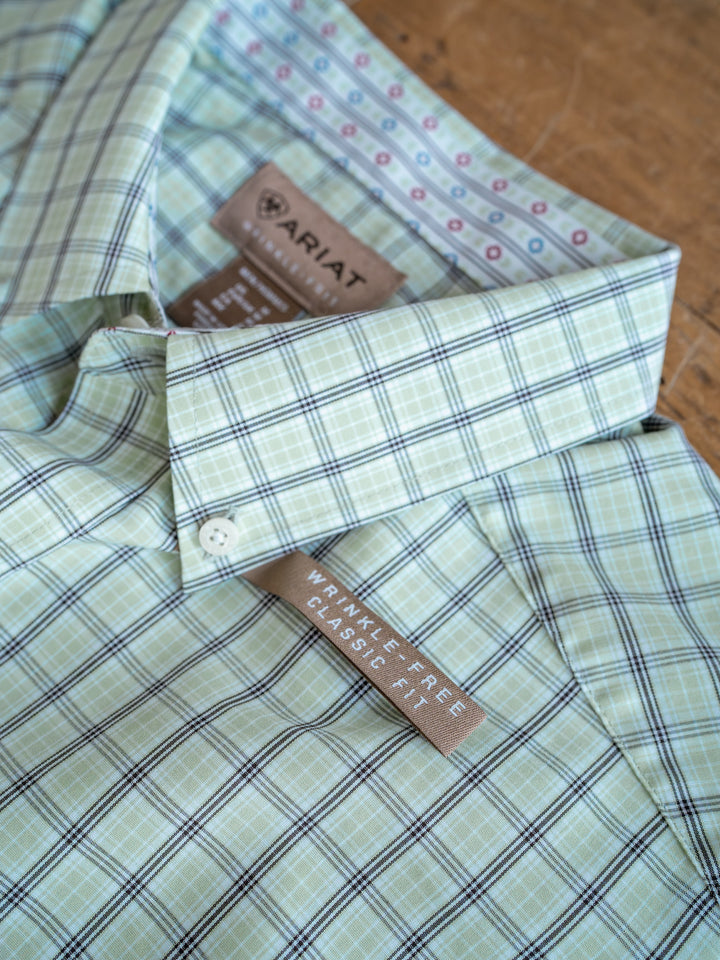 A close-up of The Graham men's plaid shirt in green and white, with tags showing the Savannah Sevens western life{&}style brand and classic fit label, displayed on a wooden surface.