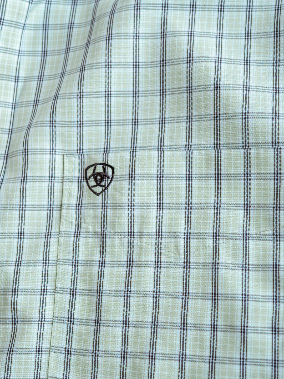 Close-up of The Graham men's plaid shirt in light green and blue by Savannah Sevens western life{&}style, with a small black embroidered logo above the chest pocket. This short sleeve button-up is wrinkle free for easy care and style.