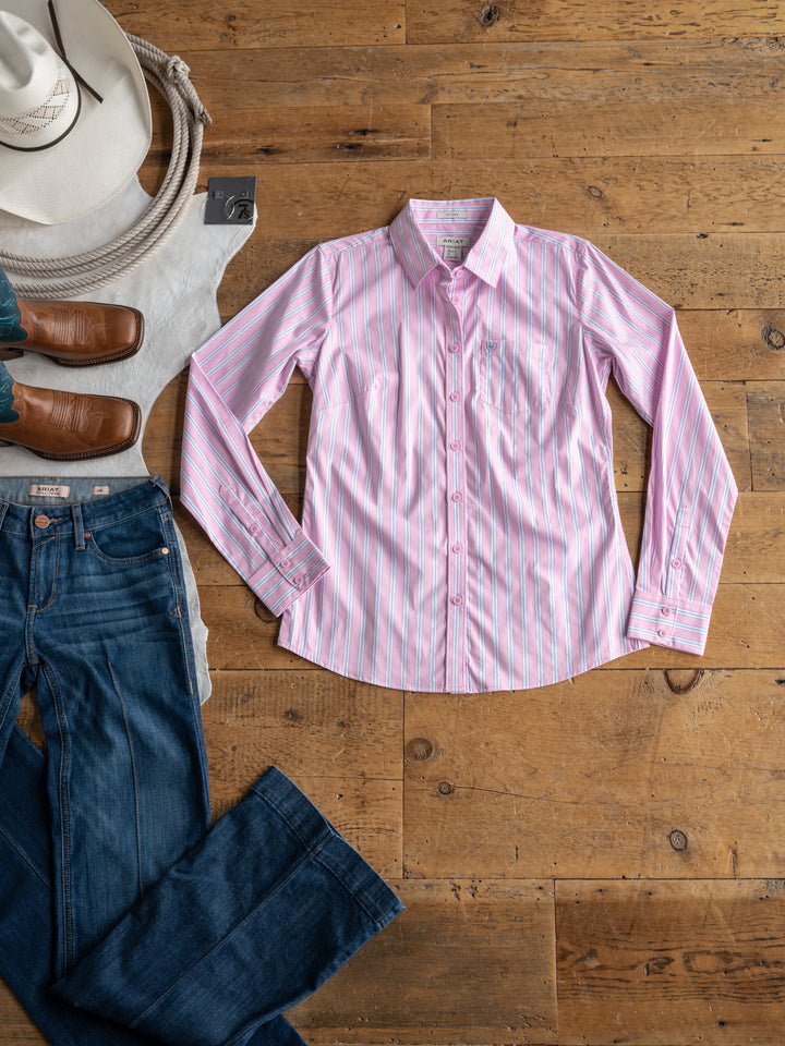 The Kinnear by Savannah Sevens western life{&}style is a pink and white striped fitted button up top, shown on a wooden floor with blue jeans, brown boots, a white hat, and beige tote bag—a polished look for stylish outings.