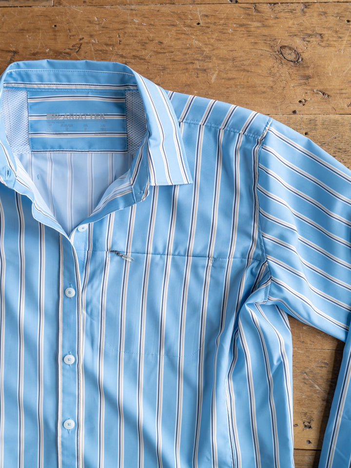 A light blue "The Colmar" long sleeve top by Savannah Sevens western life{&}style with white and navy stripes is laid flat on a wooden surface, showing the collar and part of the left sleeve for style and moisture-wicking comfort.