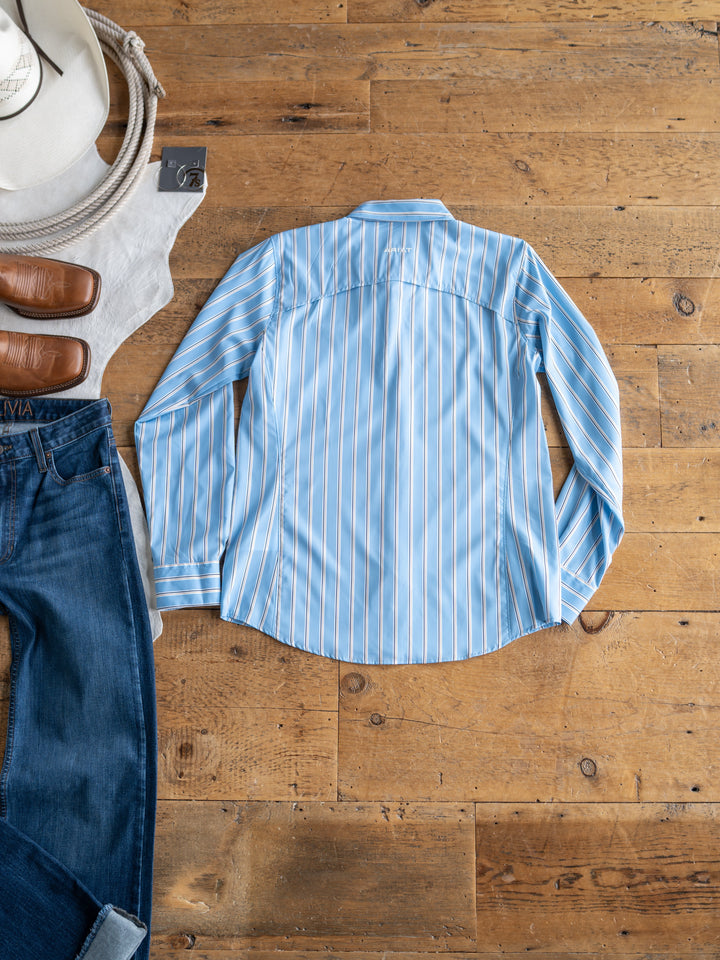 A light blue The Colmar long sleeve top by Savannah Sevens western life{&}style with white pinstripes lies on a wooden floor, paired with jeans, brown shoes, a white cowboy hat, and coiled rope. This stylish sun shirt delivers comfort and protection.
