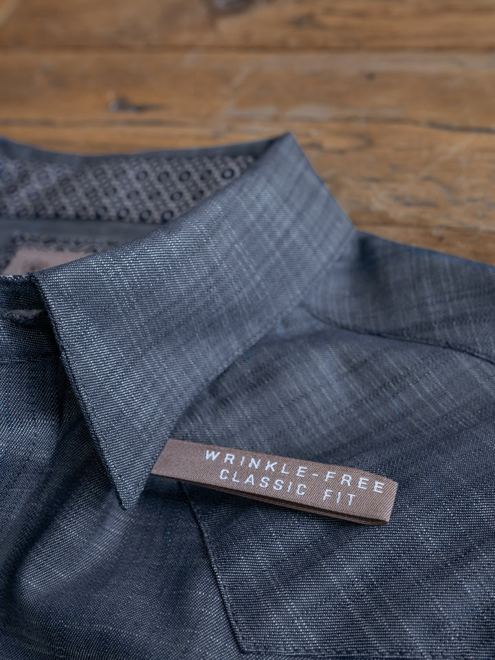 A close-up of The Elkport Men’s wrinkle-free cotton shirt by Savannah Sevens western life&style, featuring a brown label reading WRINKLE FREE CLASSIC FIT, displayed on a wooden surface.