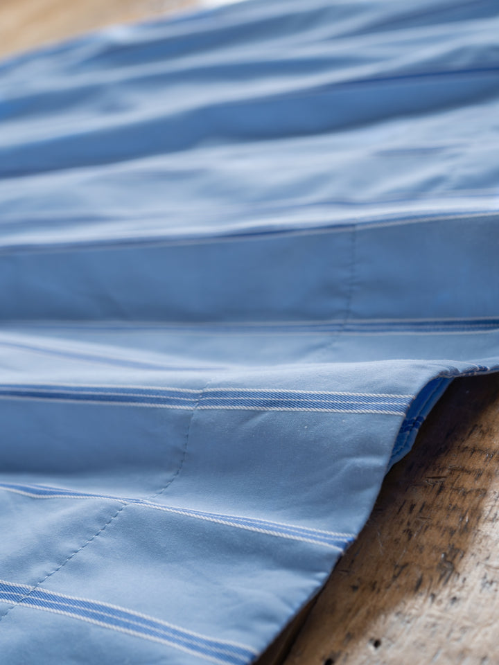 A close-up of The Berkeley by Savannah Sevens western life{&}style shows its blue striped fabric with white stitching, neatly sewn seams, and parallel lines, draped over a wooden surface.