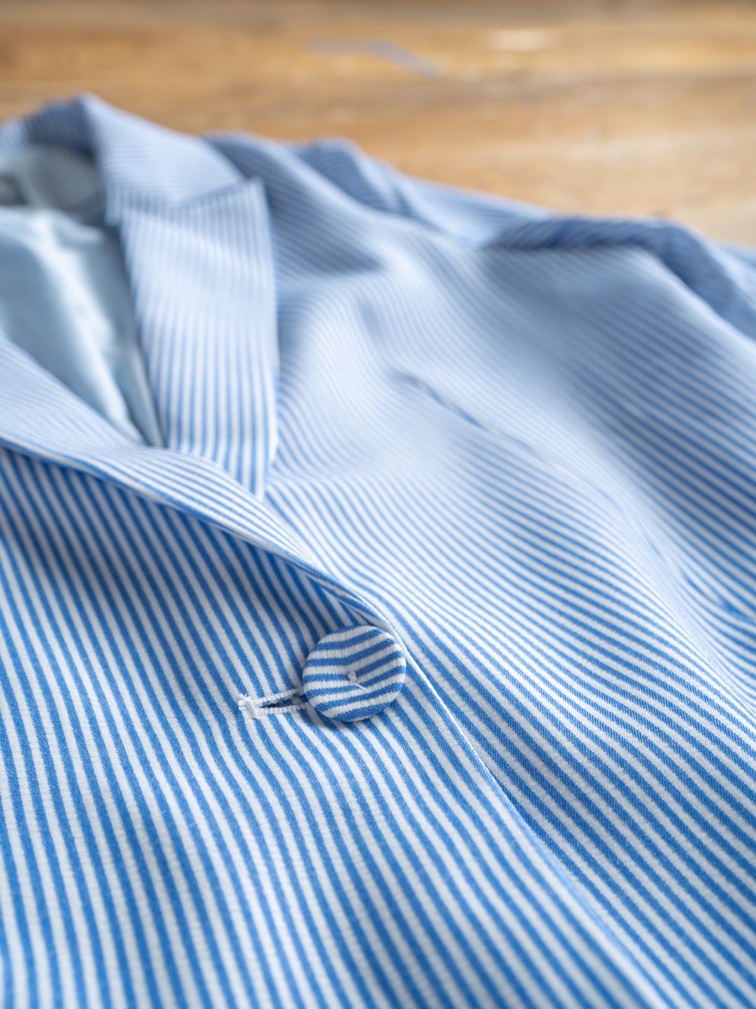 A close-up of The Malin {Set} by Savannah Sevens western life{&}style—a chic blue and white pinstripe blazer with notched lapel and single button fastening, laid flat on wood, part of a matching blazer and shorts set.