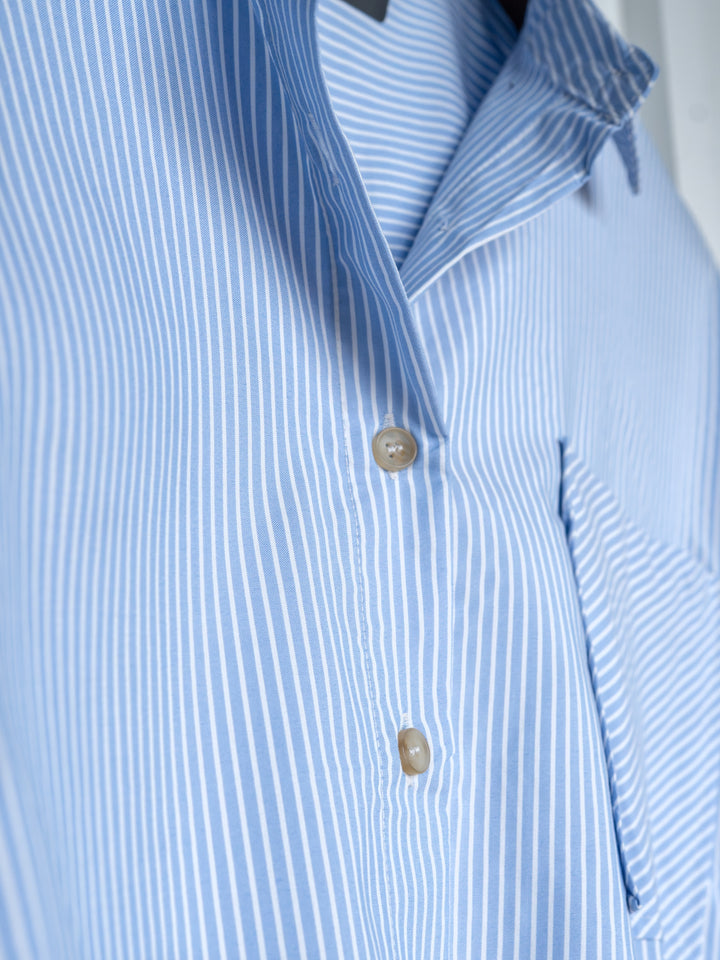 A close-up of The Driscoll by Savannah Sevens western life{&}style, featuring an ice blue and white pinstripe button-up top with two beige buttons and a partial chest pocket.