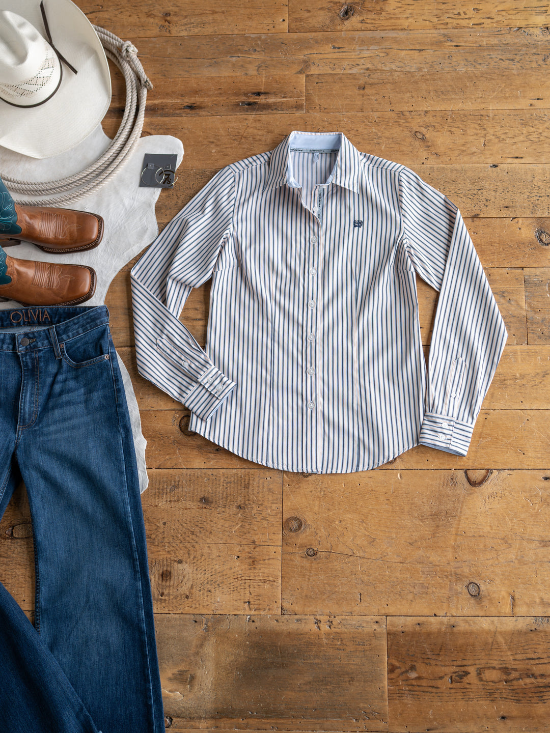 The Durant tencel top by Savannah Sevens western life&style is shown on a wooden floor with blue jeans, brown leather shoes, a cream hat, and a folded white sweater.