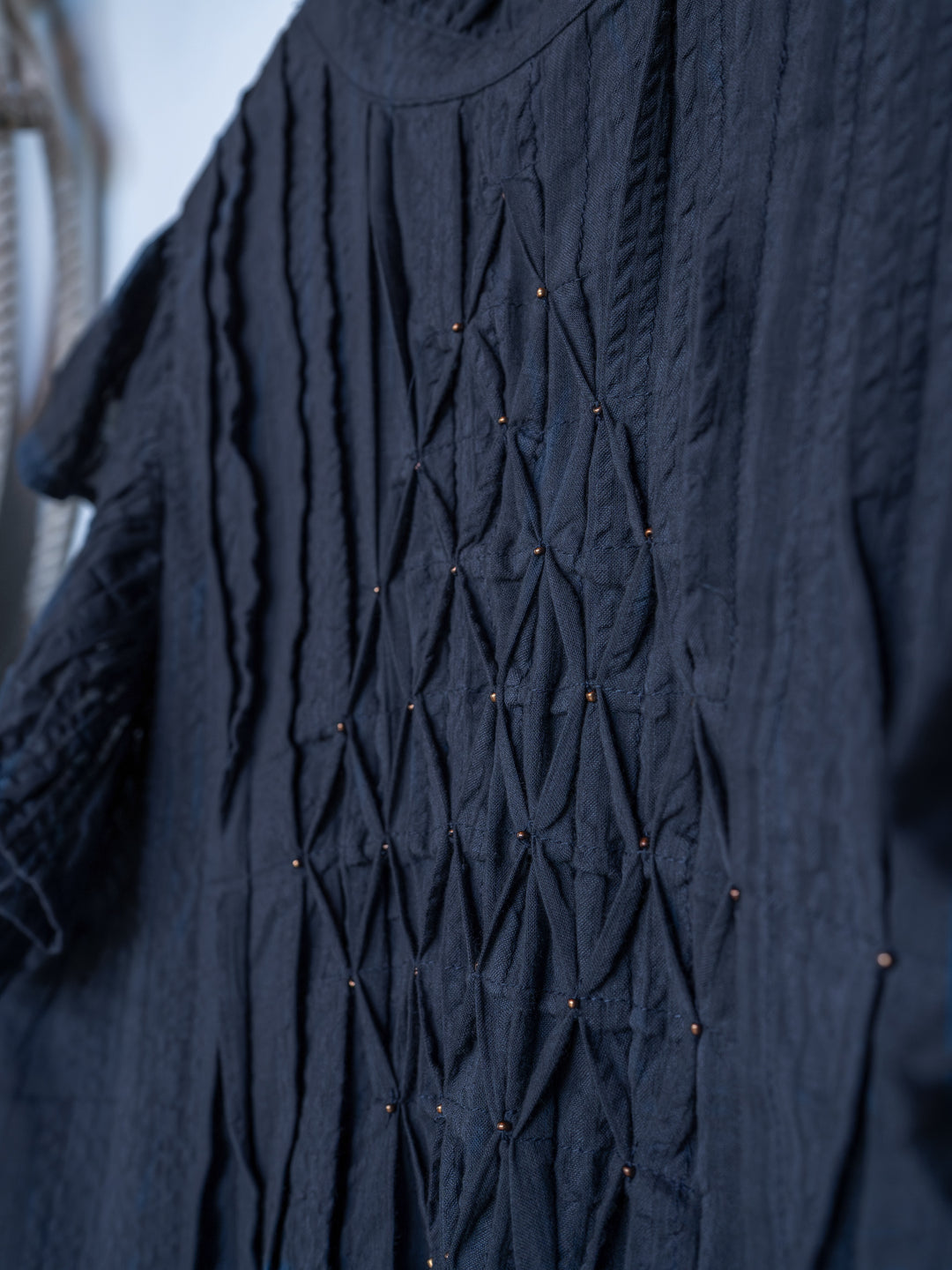 Close-up of The Winnett by Savannah Sevens western life{&}style, a midnight navy short sleeve top with intricate geometric smocking and small decorative beads creating a diamond pattern on the front.
