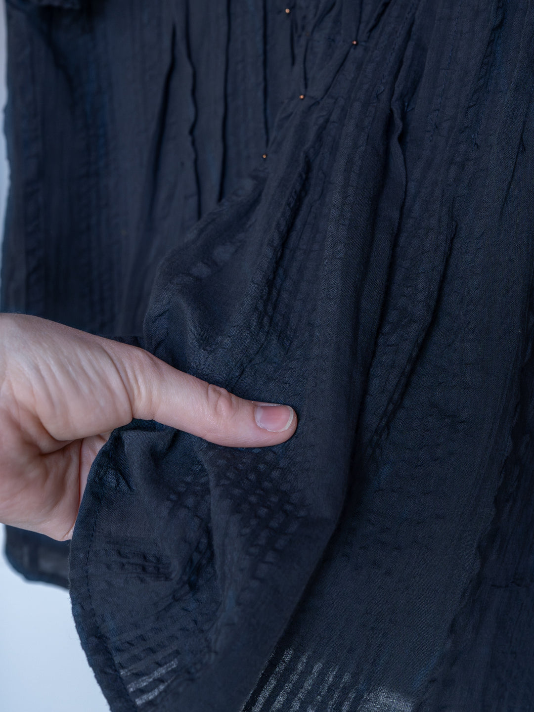 A close-up of a hand pinching the edge of The Winnett short sleeve top by Savannah Sevens western life{&}style, showcasing its midnight navy textured fabric with subtle patterns and pleats.