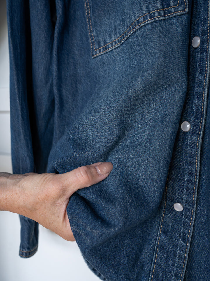 A hand rests in the side pocket of The Sorento by Savannah Sevens western life{&}style, showcasing its textured blue denim, silver snap buttons, and subtle western yoke detailing.
